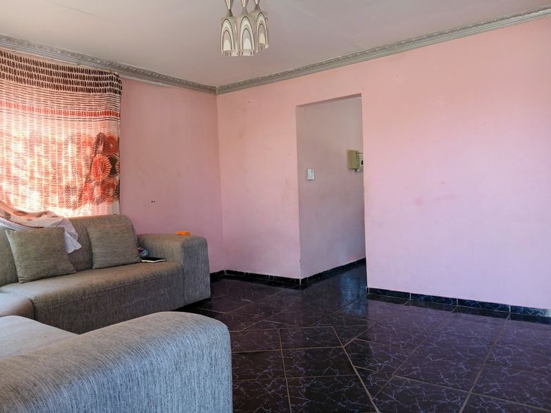 A living room featuring dark tiled flooring and decorative ceiling cornicing, requiring cosmetic updates to the wall finishes.