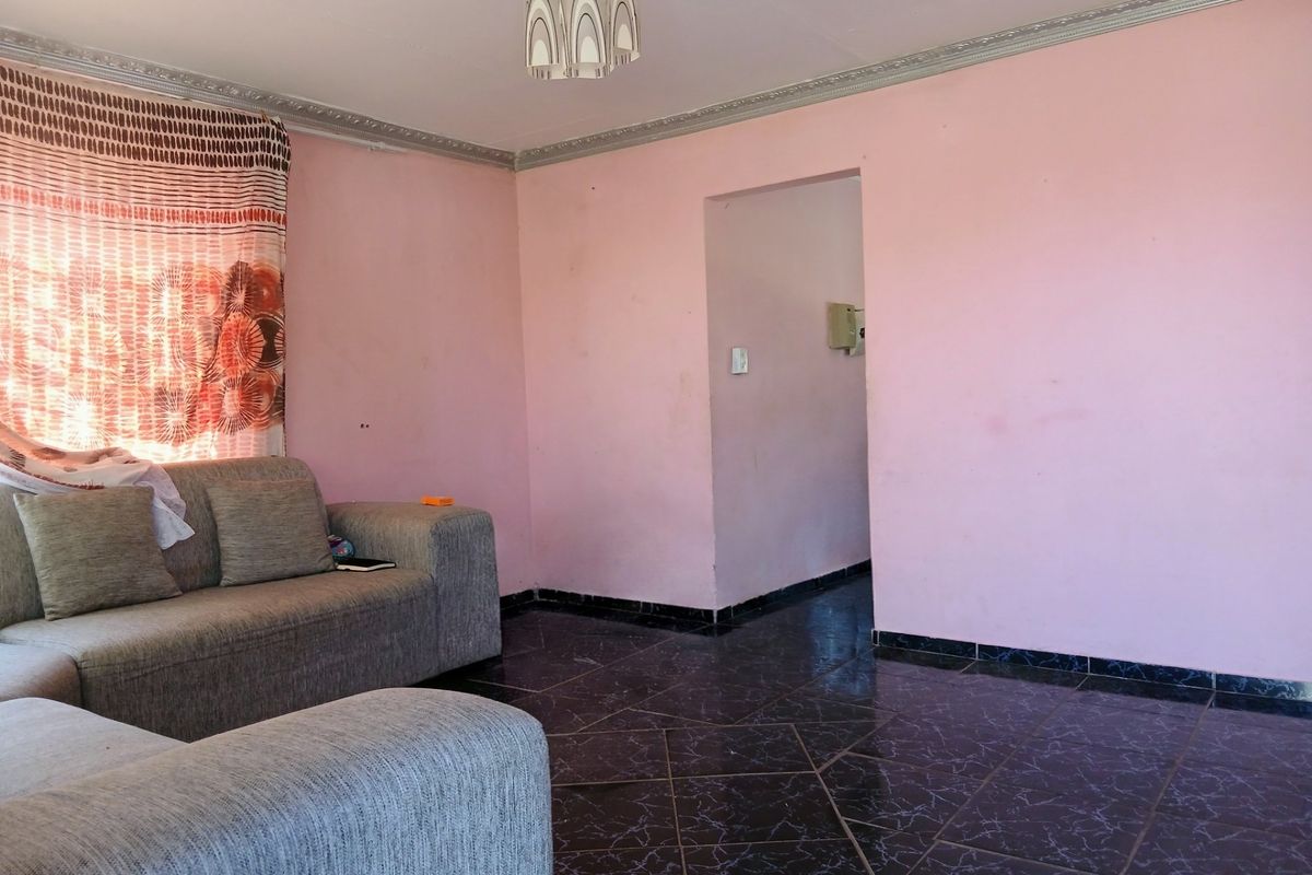 A living room featuring dark tiled flooring and decorative ceiling cornicing, requiring cosmetic updates to the wall finishes.