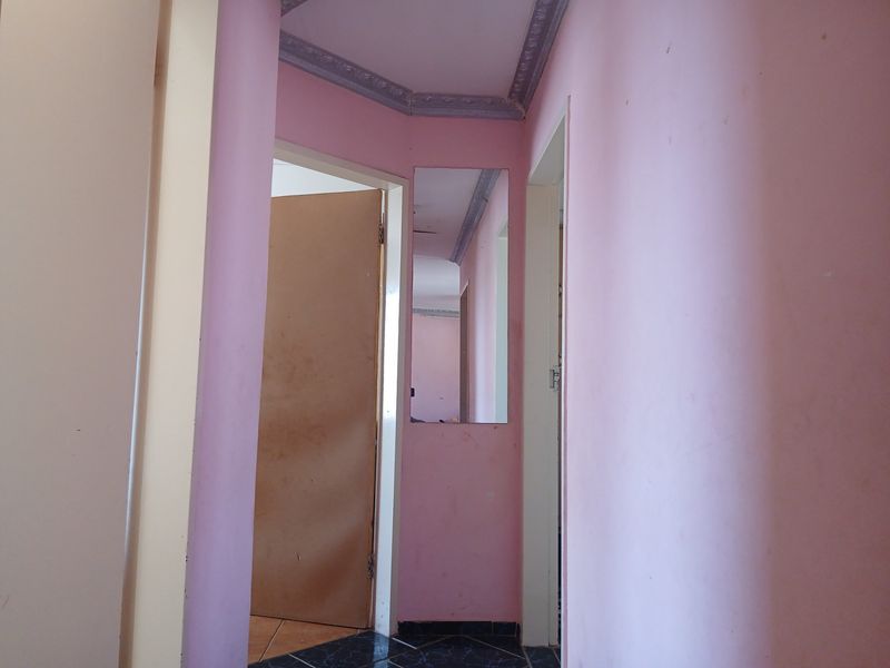 A narrow hallway featuring pink painted walls, crown molding, a built-in wall mirror, and dark tiled flooring.