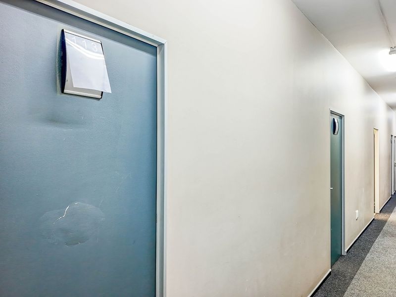 A commercial hallway featuring multiple doors, carpeted flooring, and overhead fluorescent lighting, showing signs of wear and tear.