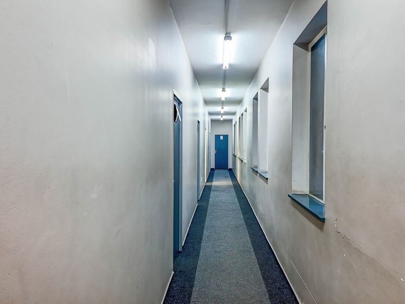 A long, functional commercial hallway featuring fluorescent strip lighting, carpeted flooring, and multiple access doors along the corridor.
