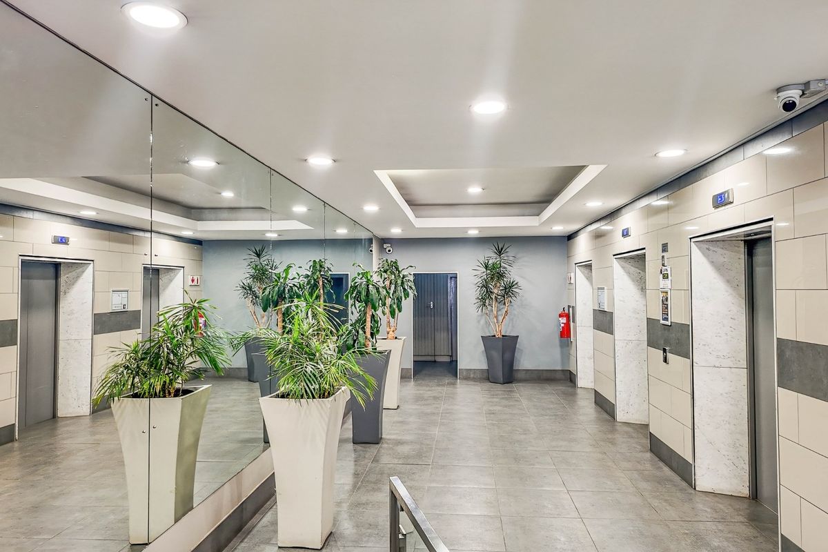 A modern commercial elevator lobby featuring tiled floors, recessed lighting, wall-to-wall mirrors, and multiple elevator access points.