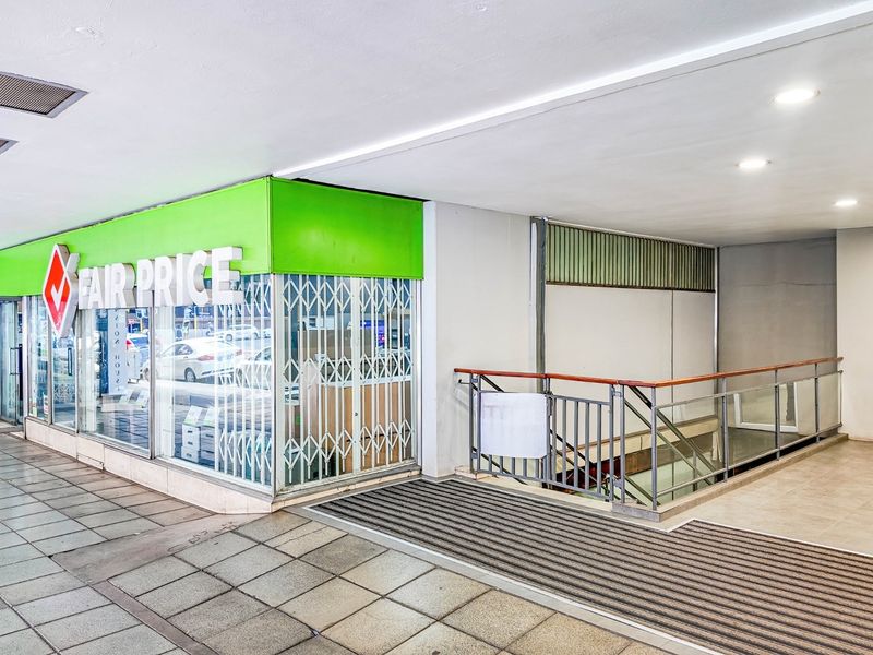 Commercial storefront entrance featuring a glass facade, metal security gate, and access to an internal staircase with a metal railing.