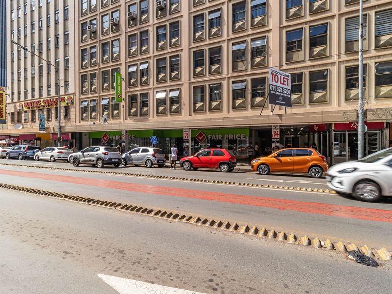 Street-level view of a multi-story commercial building featuring ground-floor retail storefronts and office space above in a busy urban setting.