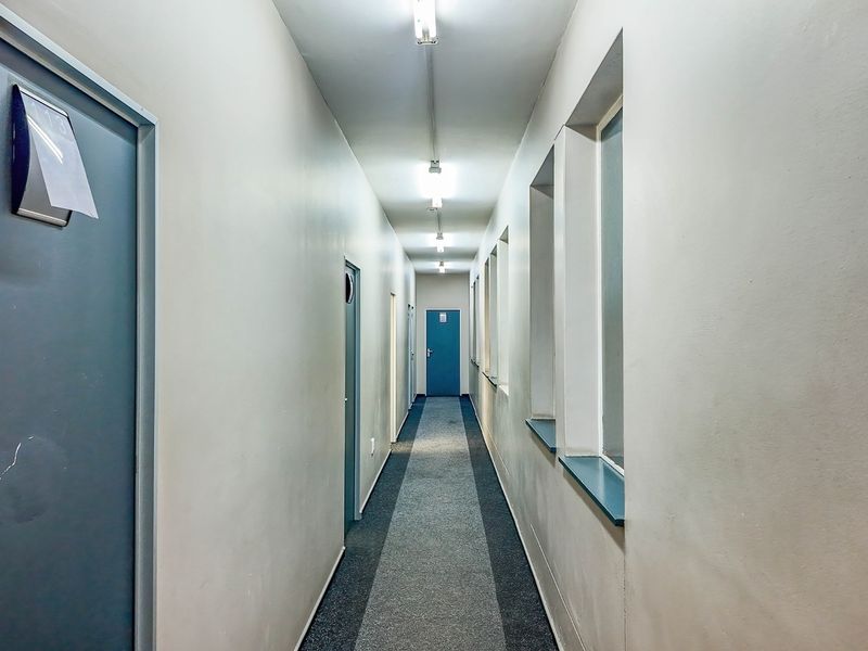 A functional commercial hallway featuring multiple internal access doors, fluorescent lighting, and carpeted flooring.