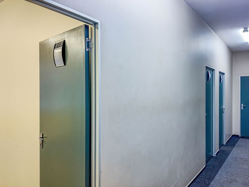 A commercial office hallway featuring multiple doors with signage, fluorescent lighting, and carpeted flooring.