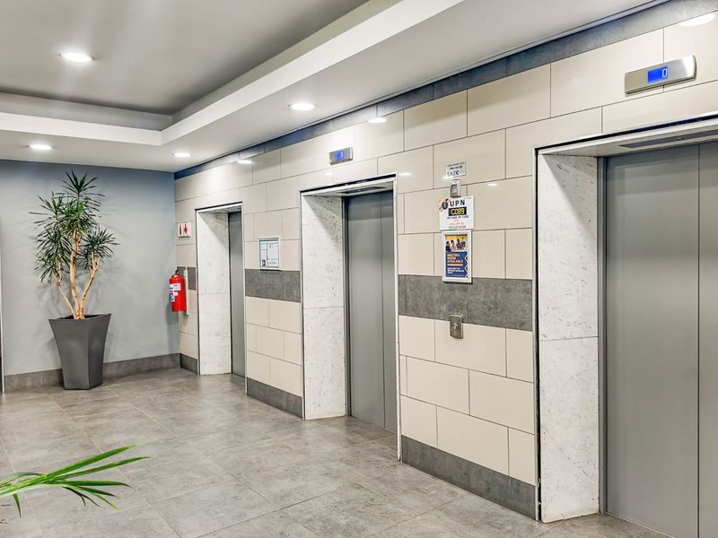 Modern commercial building elevator lobby featuring tiled walls, grey floor tiles, and recessed ceiling lighting.