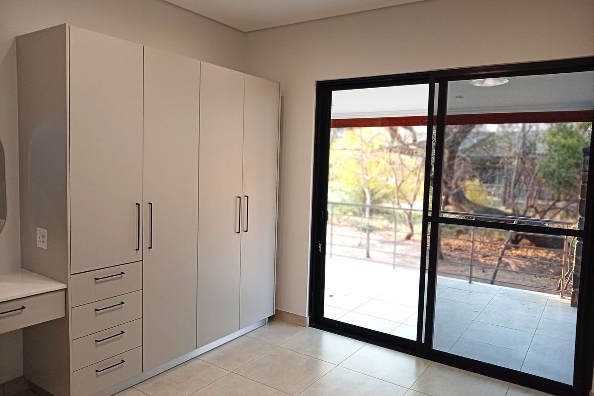 A bright, modern bedroom featuring neutral built-in cabinetry, a vanity unit, and large sliding glass doors that open onto a private patio area.