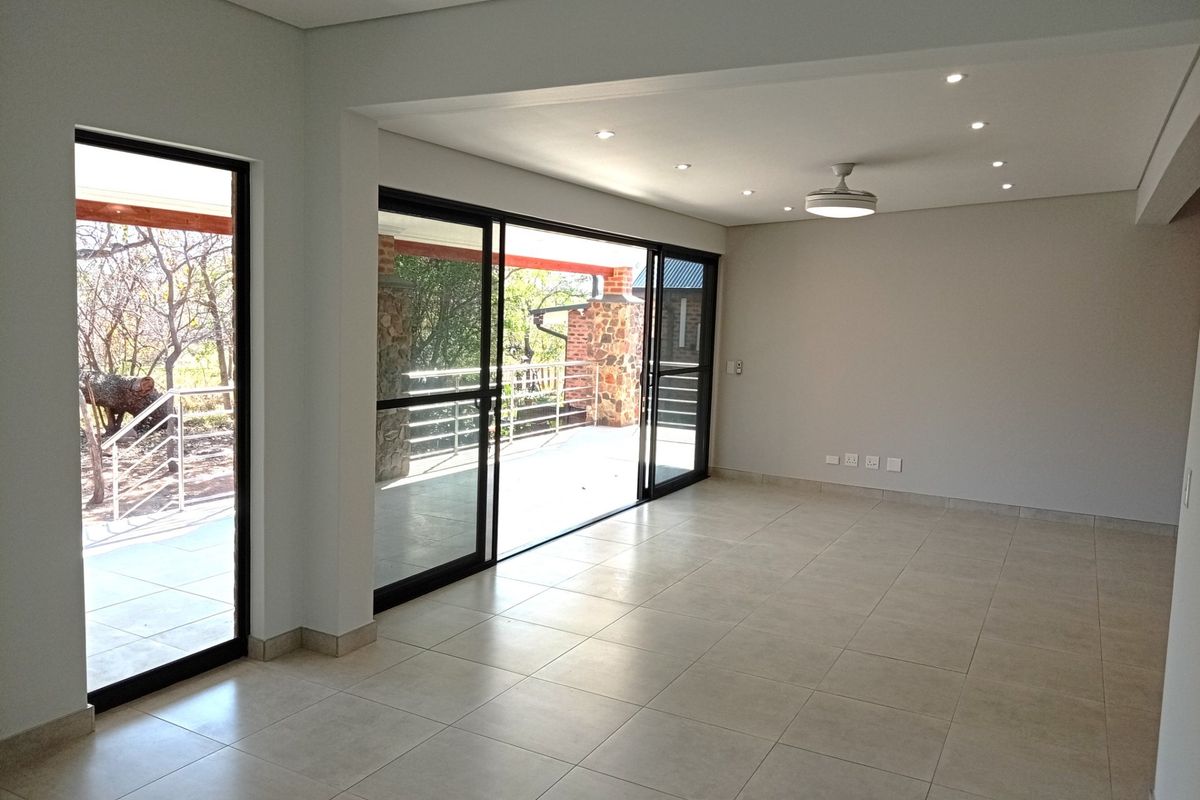 A bright, spacious, and empty living area featuring neutral tiled flooring, recessed lighting, and large sliding glass doors leading to an outdoor patio.