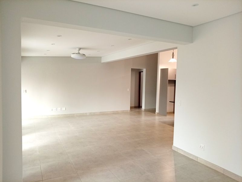 A spacious, neutral open-plan living area featuring modern tiled flooring, recessed lighting, and a ceiling fan, offering a clean canvas for interior design.