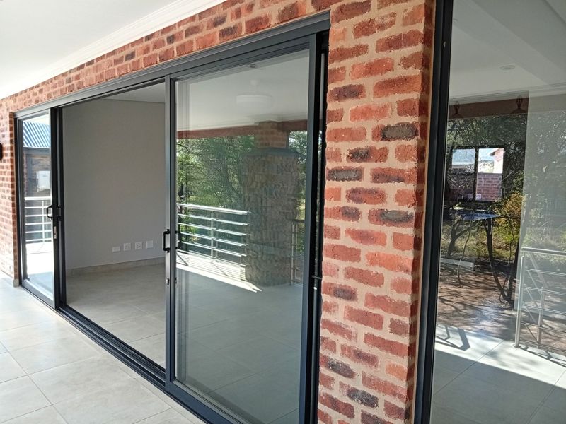 A covered patio area featuring exposed brick walls, large sliding glass doors, and tiled flooring, offering a seamless transition to the outdoor space.