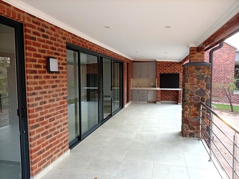 A spacious covered patio featuring exposed brickwork, a stone-clad pillar, built-in braai, outdoor cabinetry, and large sliding glass doors leading to the interior.