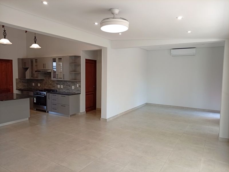 Spacious open-plan living area featuring neutral tiled flooring, modern kitchen cabinetry with stone countertops, and a wall-mounted air conditioning unit.