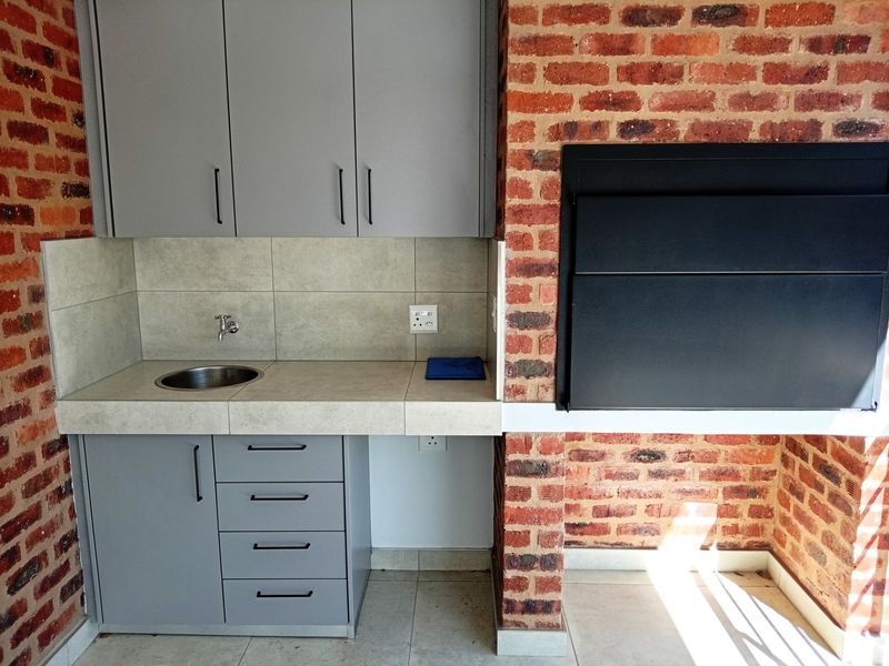 Covered patio area featuring a built-in braai, grey cabinetry, stainless steel sink, and exposed brick wall finishes.