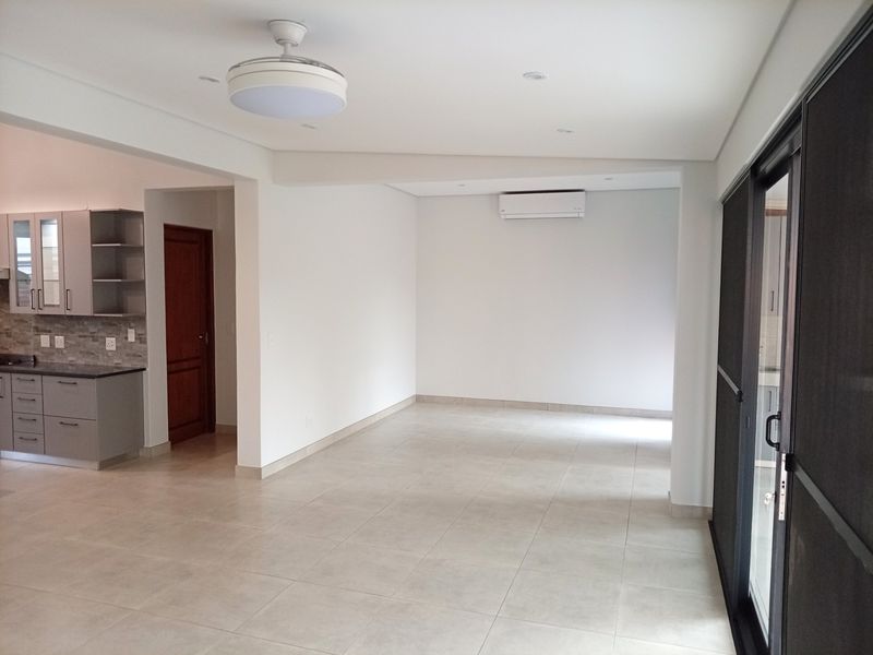 Spacious open-plan living area featuring neutral tiled floors, modern kitchen cabinetry, split-system air conditioning, and large sliding doors leading to outdoor space.