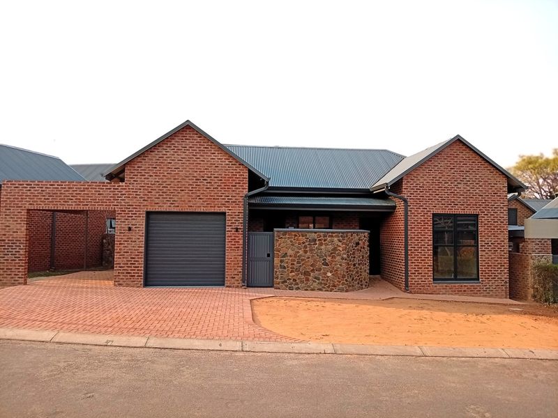 Front elevation of a modern brick retirement village unit featuring a single garage, stone accent wall, and paved driveway with unfinished garden area.