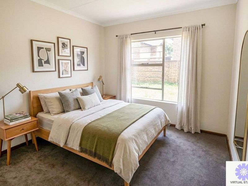 A well-lit bedroom featuring neutral wall tones, carpeted flooring, and a large window with curtain tracks, providing a comfortable and inviting living space.