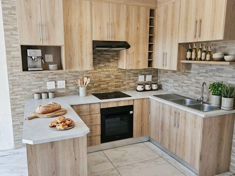 Modern kitchen featuring light wood-grain cabinetry, stone-look tiled backsplash, integrated electric hob and oven, and marble-effect floor tiles.