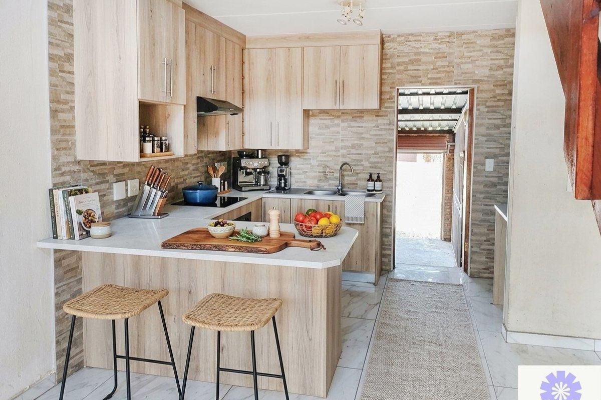 Modern kitchen featuring light wood cabinetry, stone countertops, integrated hob and extractor, and stylish tiled backsplash with direct access to the rear exterior.