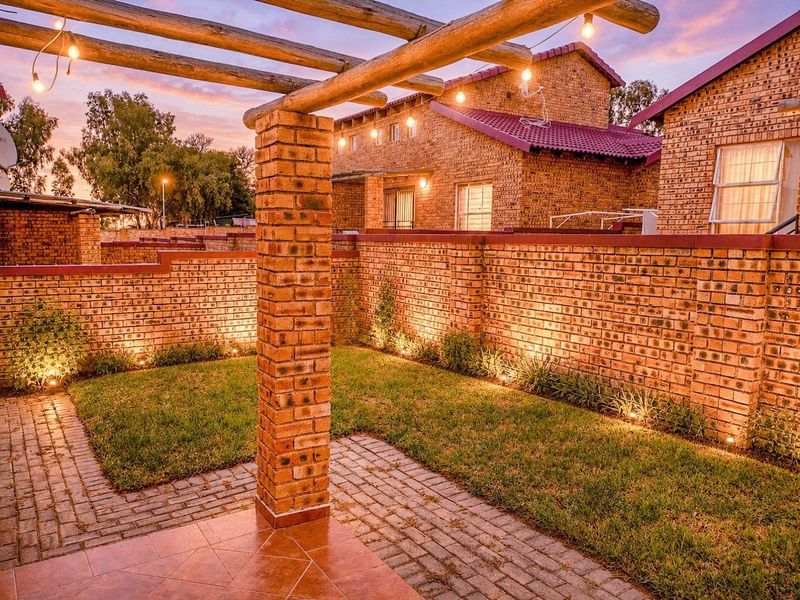 A well-maintained rear garden featuring a brick boundary wall, paved patio area, and a timber pergola with integrated outdoor lighting.