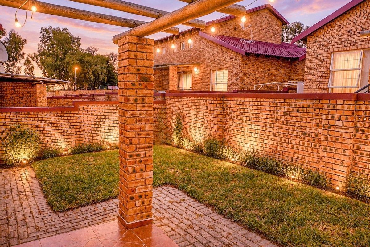 A well-maintained rear garden featuring a brick boundary wall, paved patio area, and a timber pergola with integrated outdoor lighting.