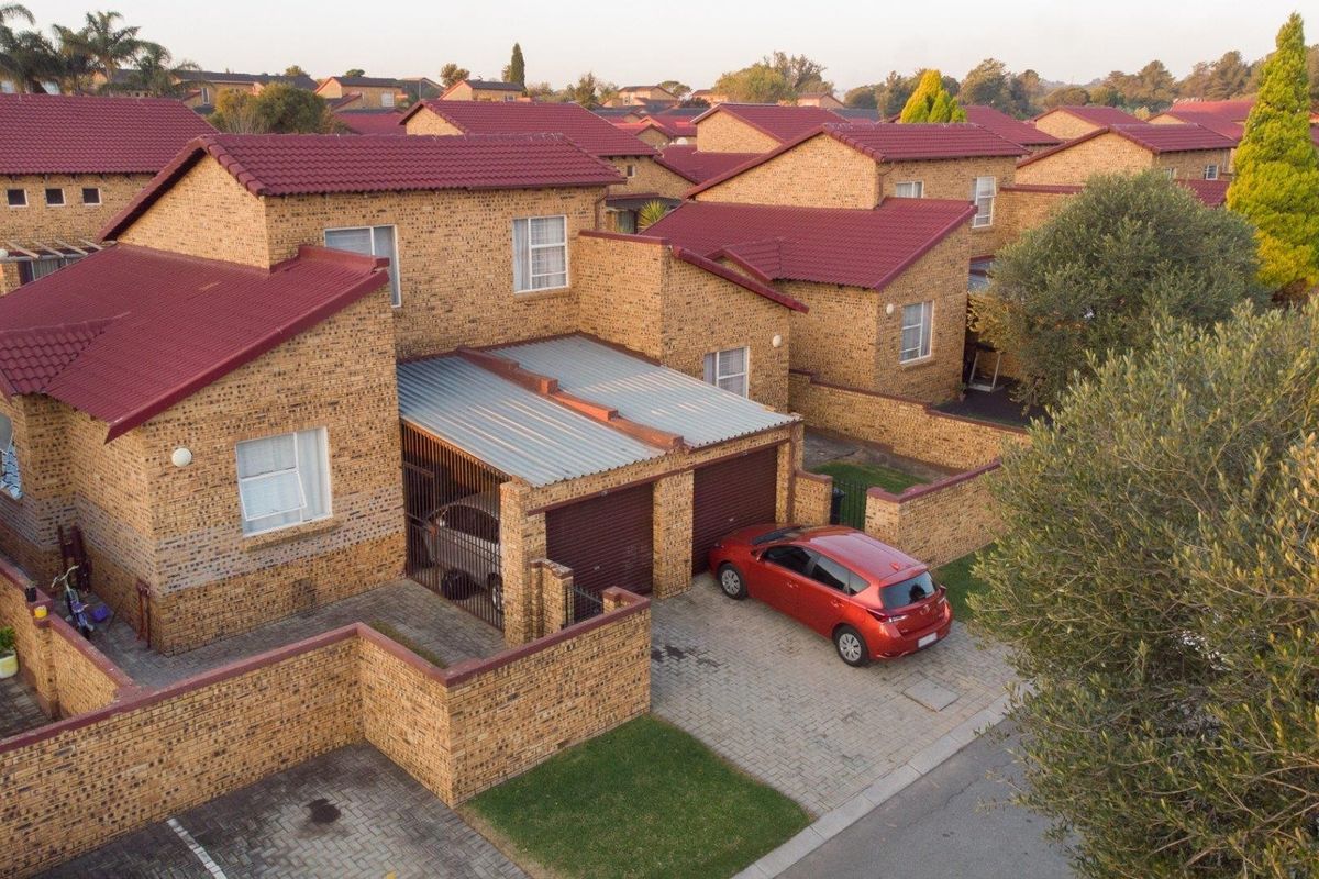 Aerial view of a facebrick townhouse complex featuring tiled roofs, double garages, and paved driveways within a residential estate setting.