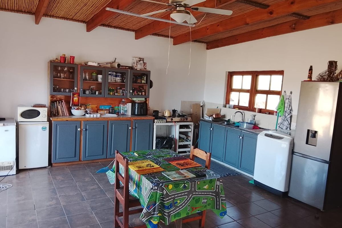 Spacious kitchen featuring exposed timber beam ceilings, bamboo paneling, tiled flooring, and ample fitted cabinetry with a double basin sink.