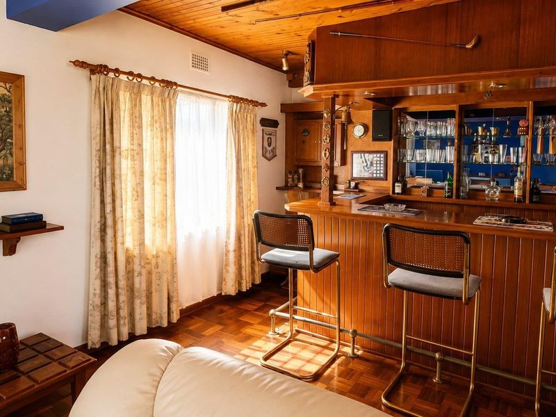 A dedicated home bar area featuring classic timber paneling, a built-in bar counter with a brass foot rail, and warm parquet flooring.
