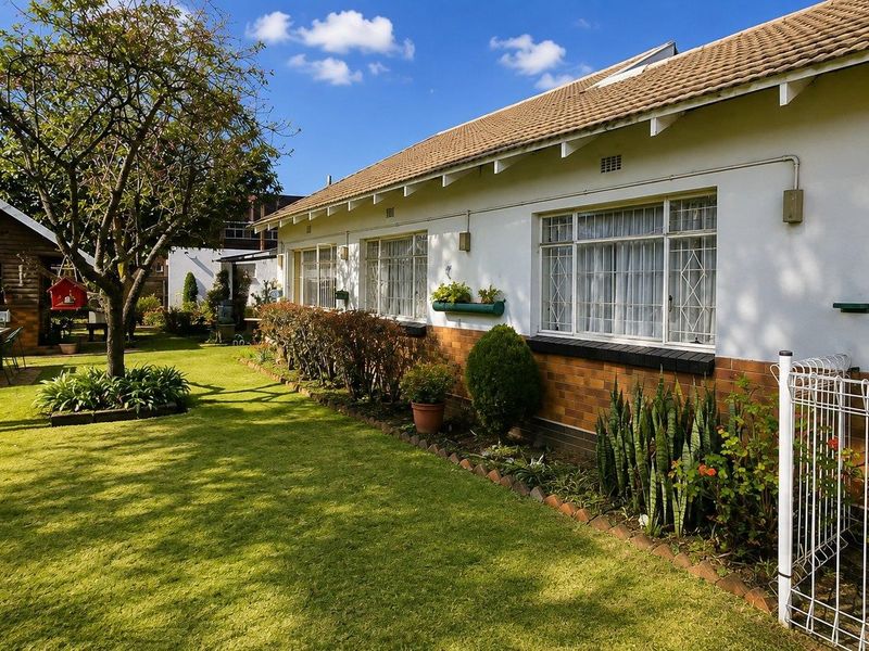 A well-maintained rear garden featuring a lawn, established landscaping, and a brick-and-tile house exterior with security-fitted windows.