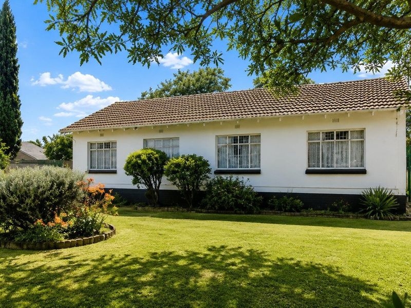A well-maintained rear exterior view of the house featuring a spacious lawn, established garden beds, and classic tiled roof architecture.