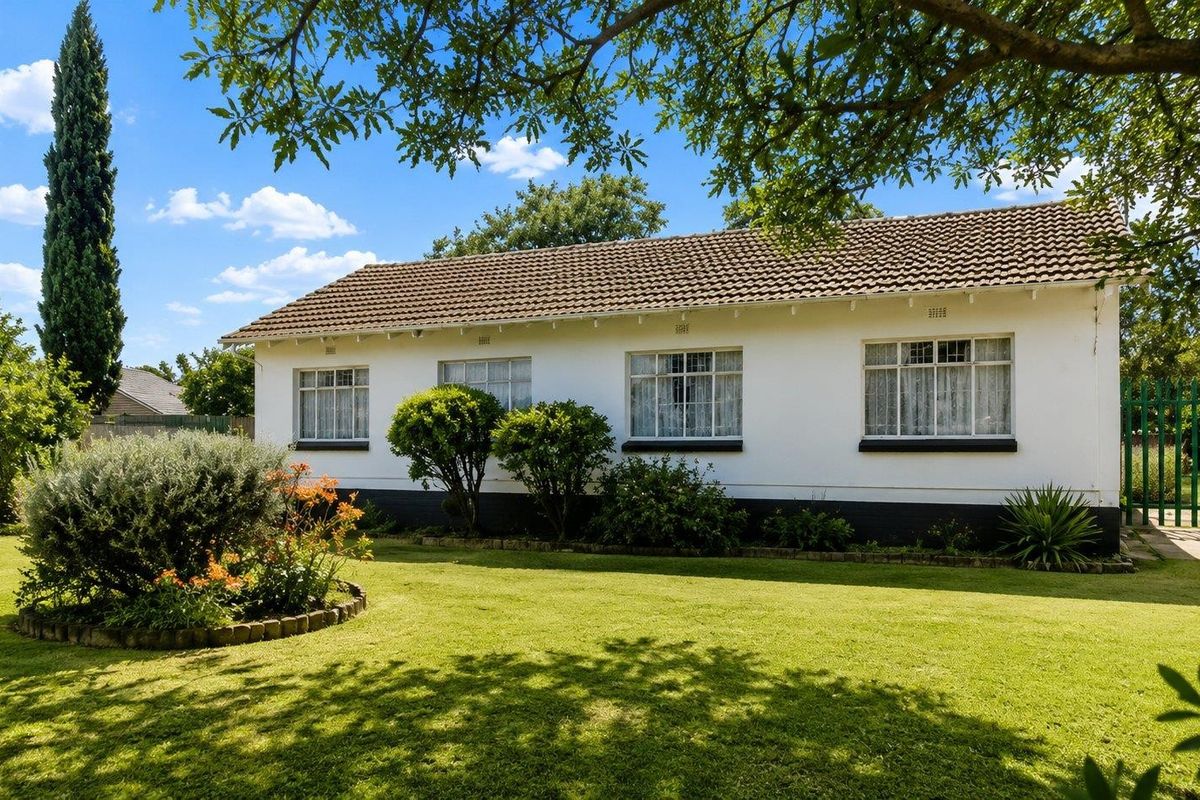 A well-maintained rear exterior view of the house featuring a spacious lawn, established garden beds, and classic tiled roof architecture.