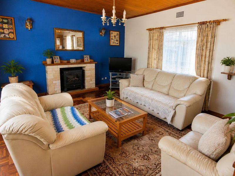 A cozy living room featuring a stone fireplace, warm timber ceilings, and classic parquet flooring, creating a traditional and inviting atmosphere.