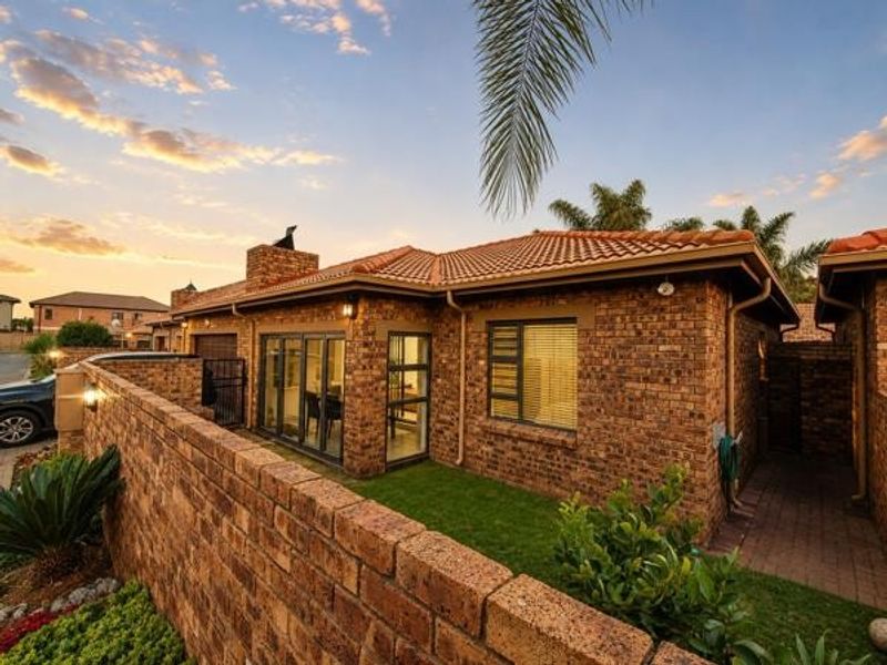 Rear view of a face brick townhouse featuring a terracotta tiled roof, aluminium window frames, sliding glass doors, and a private garden area.