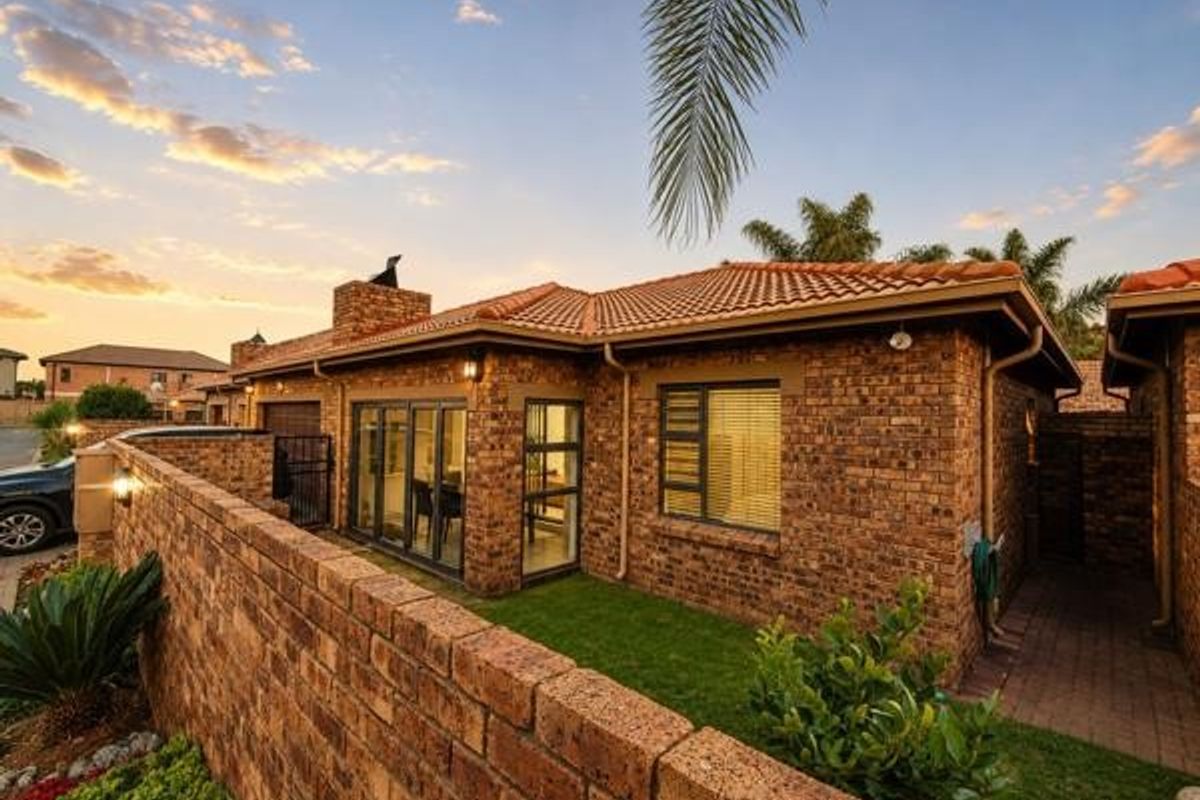 Rear view of a face brick townhouse featuring a terracotta tiled roof, aluminium window frames, sliding glass doors, and a private garden area.