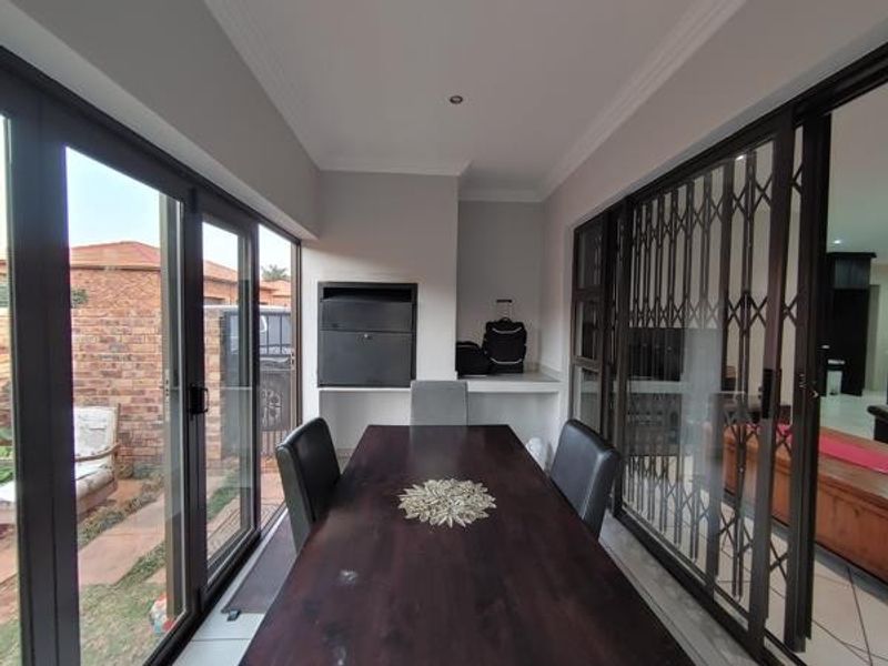 A covered patio area featuring a built-in braai, tiled flooring, and large sliding glass doors that provide access to the garden.