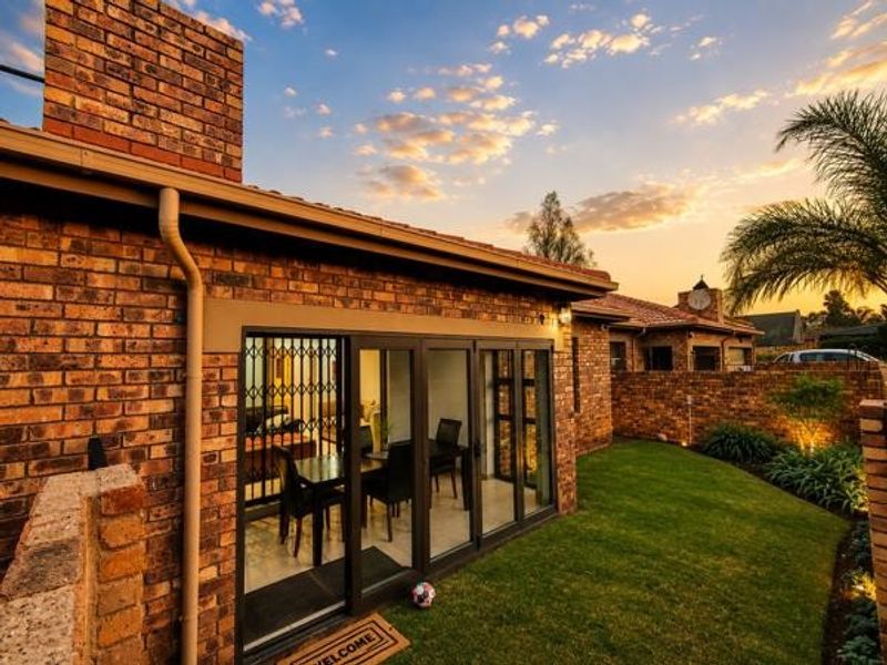 Rear view of a townhouse featuring a face brick facade, folding glass doors leading to the interior, and a well-maintained private garden.