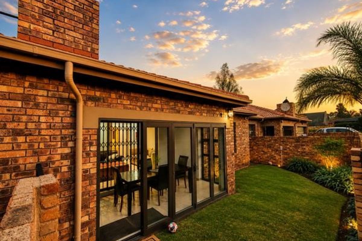 Rear view of a townhouse featuring a face brick facade, folding glass doors leading to the interior, and a well-maintained private garden.