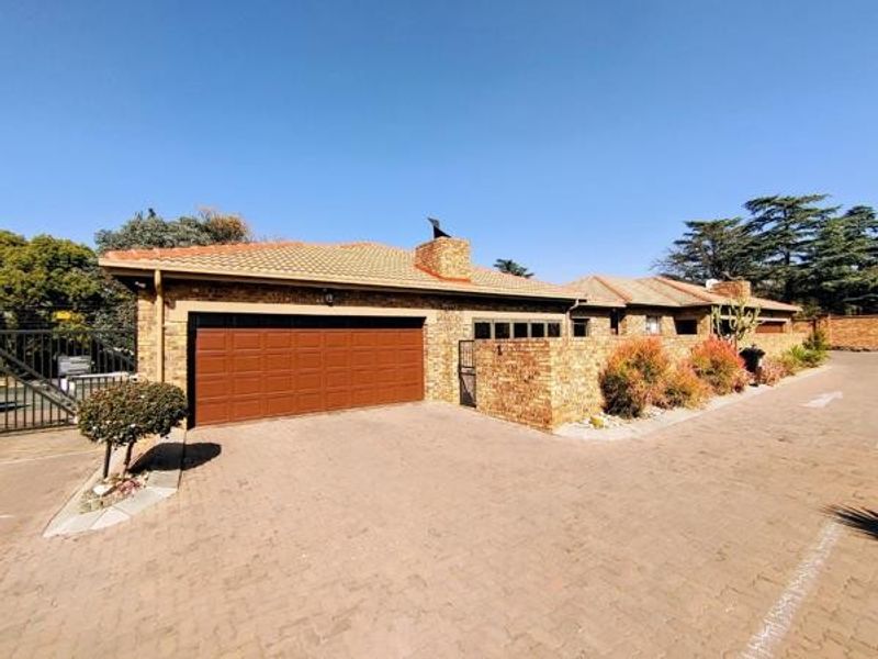 Front exterior view of a townhouse featuring a brick facade, tiled roof, and a spacious paved driveway leading to a sectional garage door.