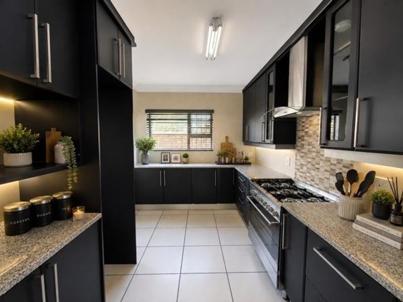 Modern kitchen featuring sleek black cabinetry, granite countertops, a gas hob with extractor fan, and a stylish mosaic tile backsplash.