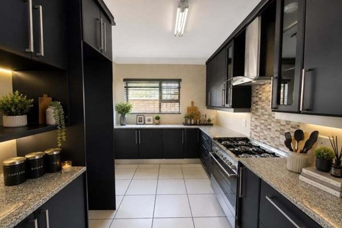 Modern kitchen featuring sleek black cabinetry, granite countertops, a gas hob with extractor fan, and a stylish mosaic tile backsplash.