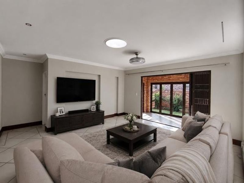 Spacious living room featuring tiled flooring, a central skylight, and large sliding glass doors that provide seamless access to the outdoor patio area.