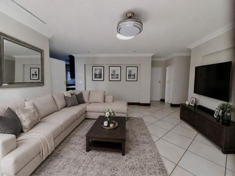 A well-maintained living room featuring neutral tiled flooring, a ceiling fan, and recessed lighting, creating a bright and comfortable living space.