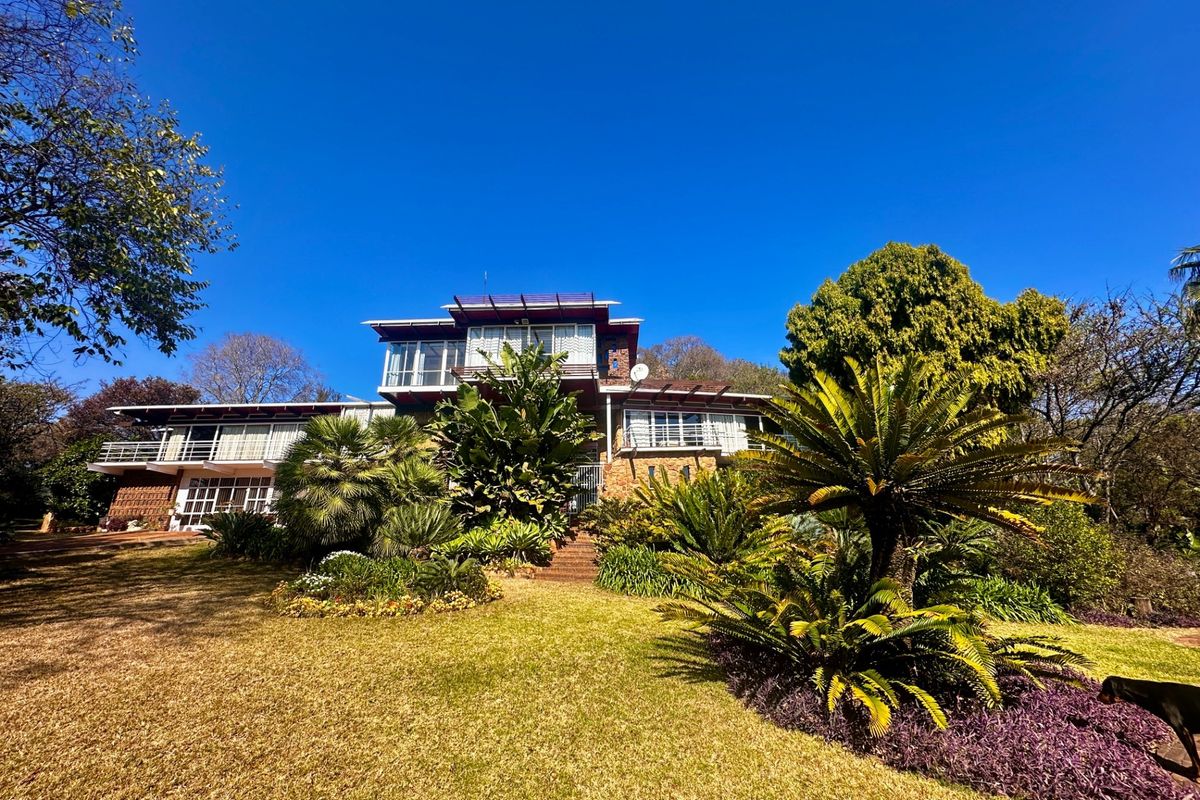 A multi-level farm residence featuring stone cladding, expansive balconies, and a well-maintained landscaped garden setting.