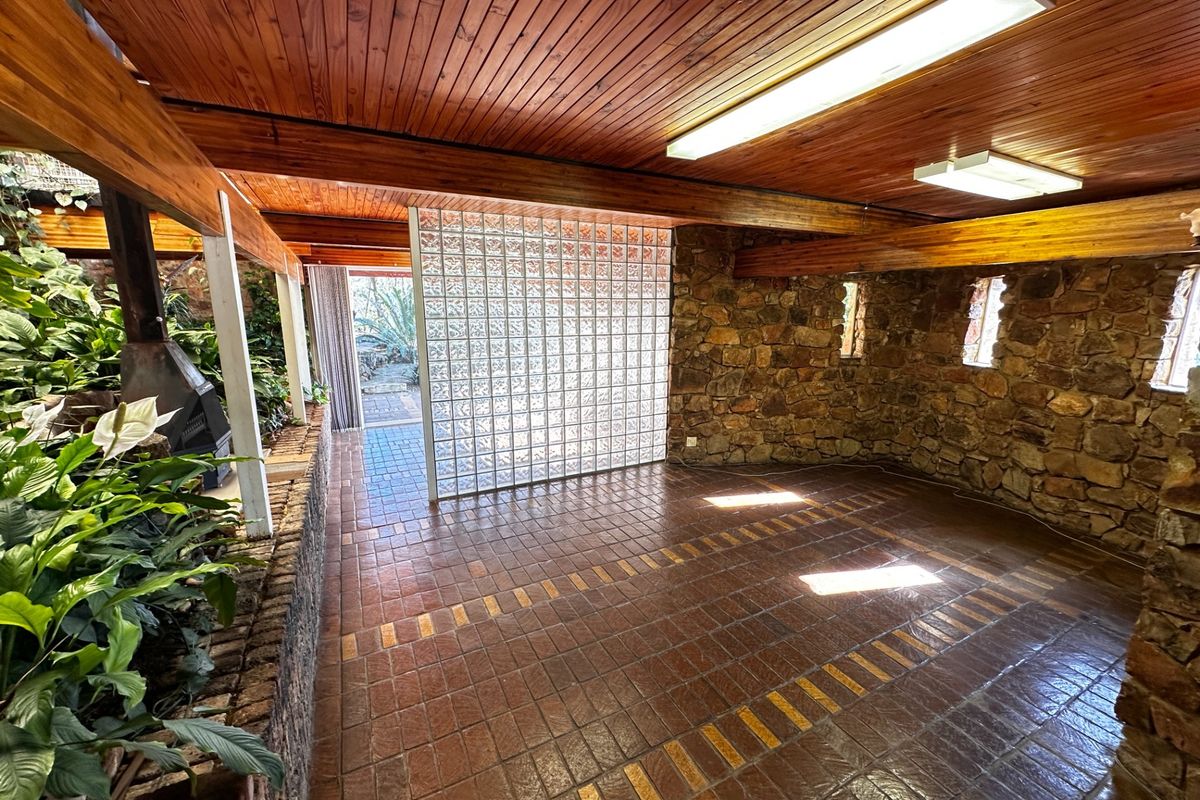 Spacious living area featuring a rustic stone wall, timber-clad ceiling, glass block partition, and terracotta tile flooring with an integrated indoor planter.