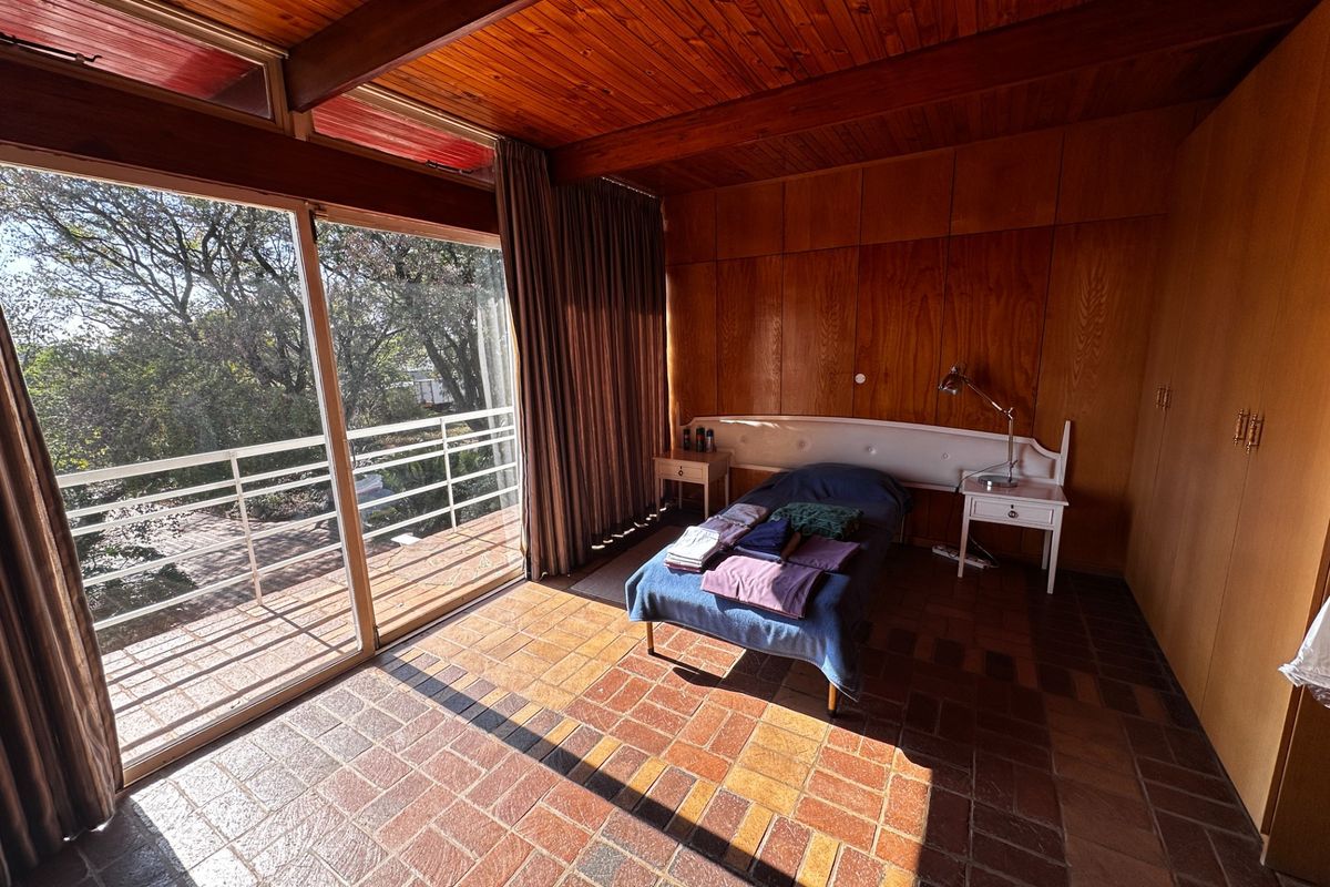 Spacious bedroom featuring warm timber-clad ceilings, wood paneling, built-in wardrobes, and terracotta tile flooring, with direct access to a private balcony.