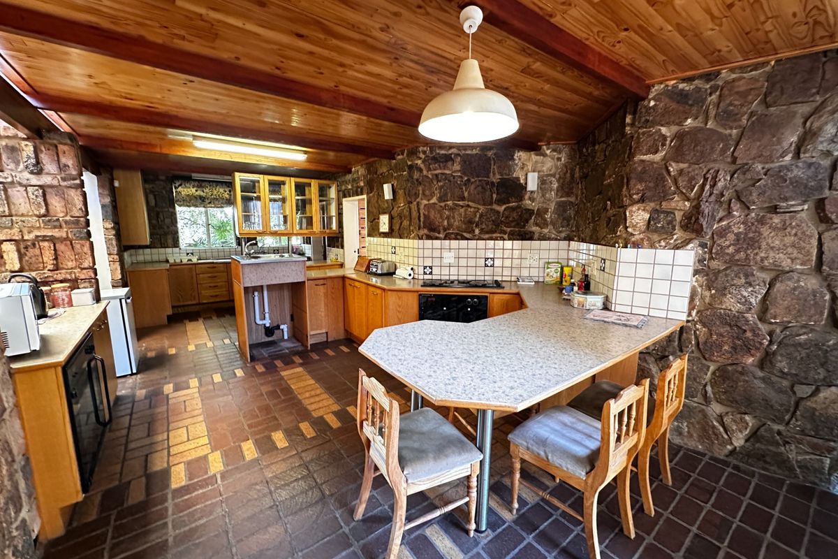 Rustic kitchen featuring stone walls, timber ceiling, tiled flooring, and built-in cabinetry with a breakfast bar area.