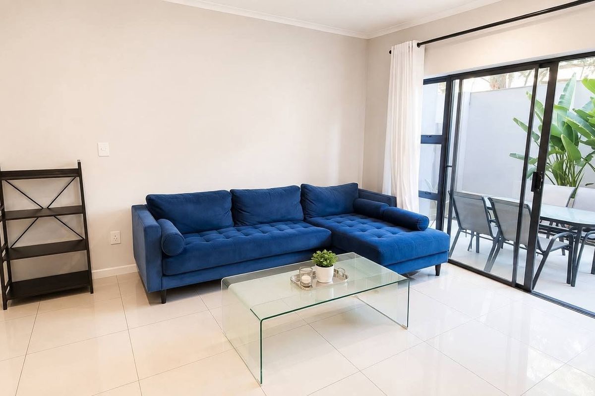 Bright living room featuring large sliding glass doors that open onto a private patio area, complemented by neutral tiled flooring.