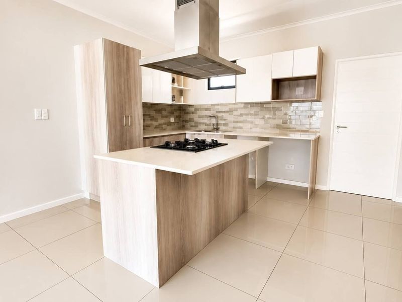 Modern kitchen featuring a central island with a gas hob, stainless steel extractor fan, ample built-in cabinetry, and neutral tiled flooring.
