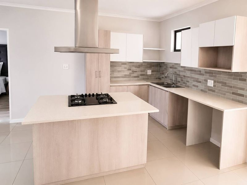 Modern kitchen featuring a central island with a gas hob, stainless steel extractor, stone countertops, and ample built-in cabinetry with a tiled backsplash.