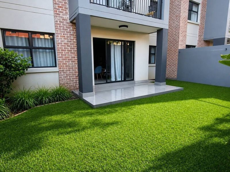 A well-maintained rear exterior view featuring a tiled patio, artificial lawn, and a modern brick and render facade with a sliding glass door.